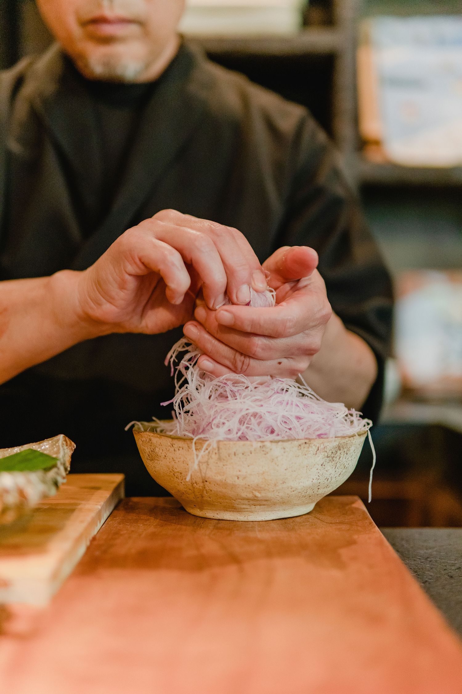 Chef preparing ingredients in a restaurant kitchen with noodles in a bowl.