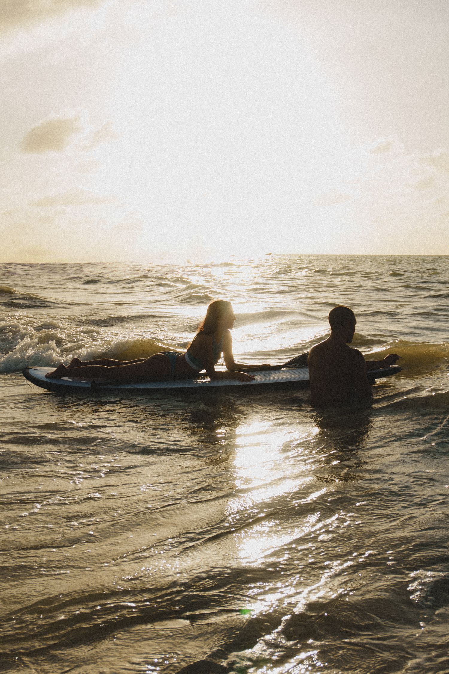 Silhouetted surfers float on surfboards in golden ocean waters during sunset.
