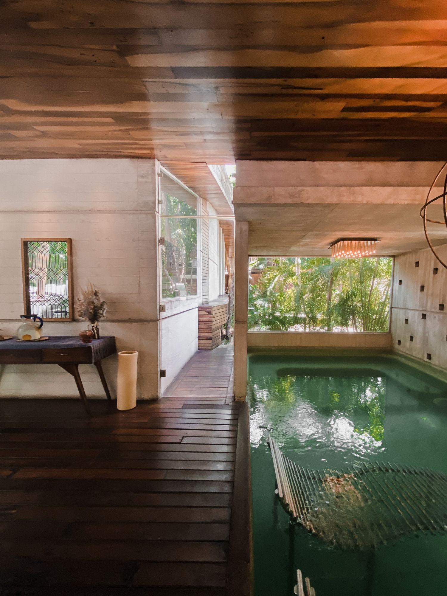 Indoor swimming pool with wooden ceiling and glass walls overlooking lush greenery creates a serene spa-like atmosphere.