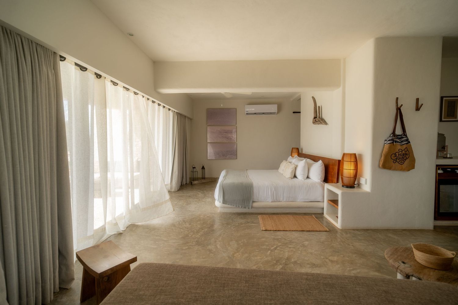 A modern minimalist interior space with white walls, light flooring, and sheer curtains creating an airy atmosphere.