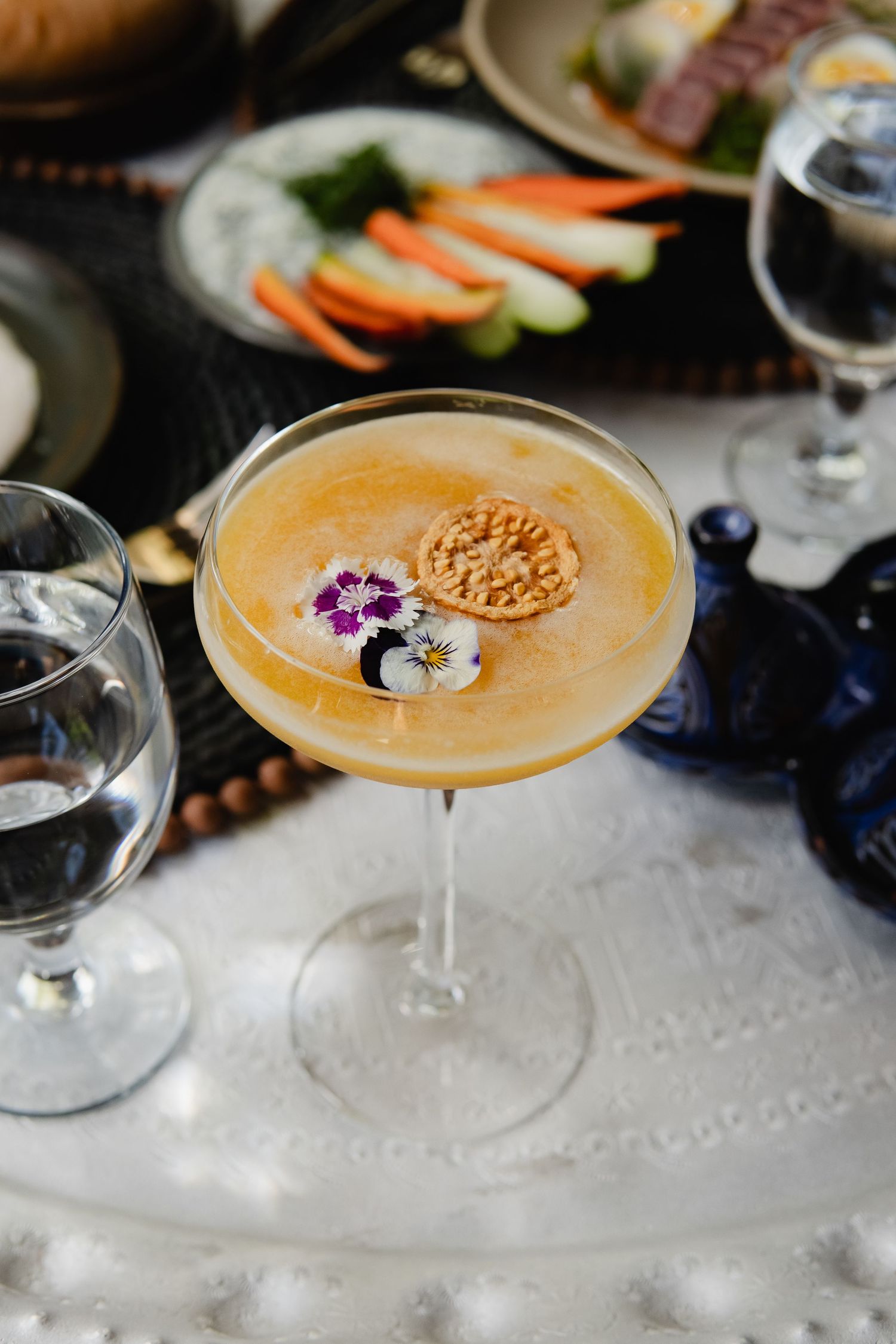 Elegant cocktail garnished with a round cookie served in a coupe glass on a textured white surface.