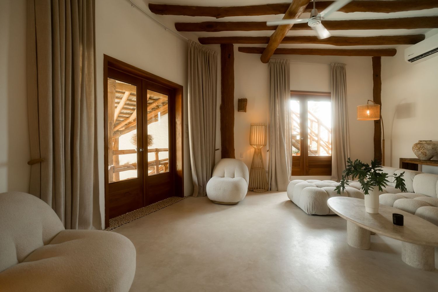 Luxurious Mediterranean villa interior with beamed ceiling, cream furnishings, and large windows overlooking scenic views.