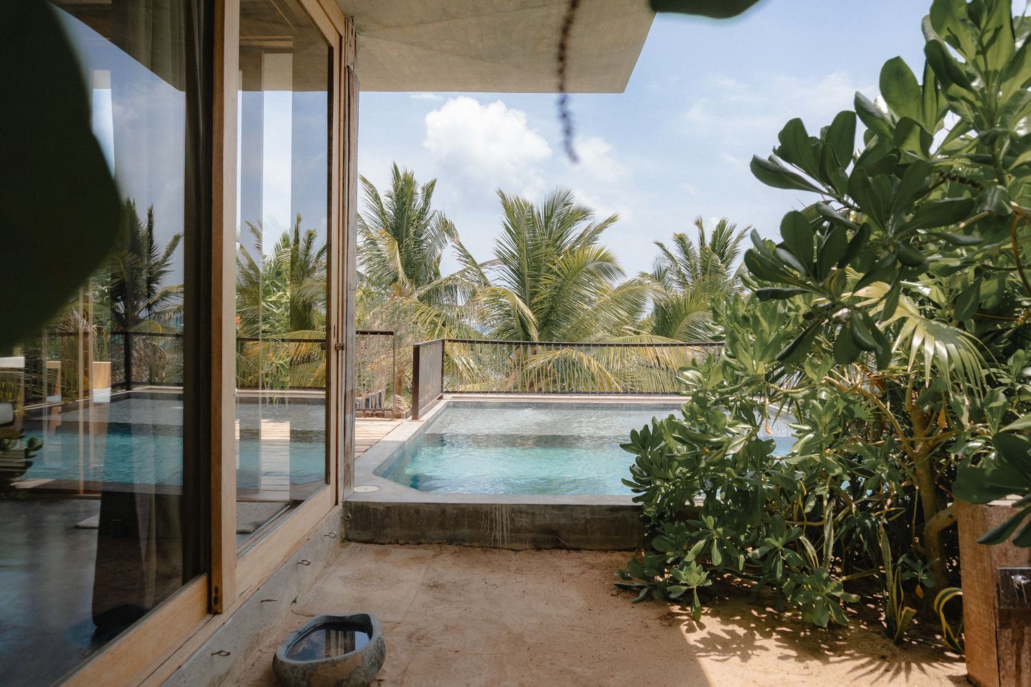 Panoramic view of a tropical beachfront resort with palm trees and modern architecture against a blue sky.