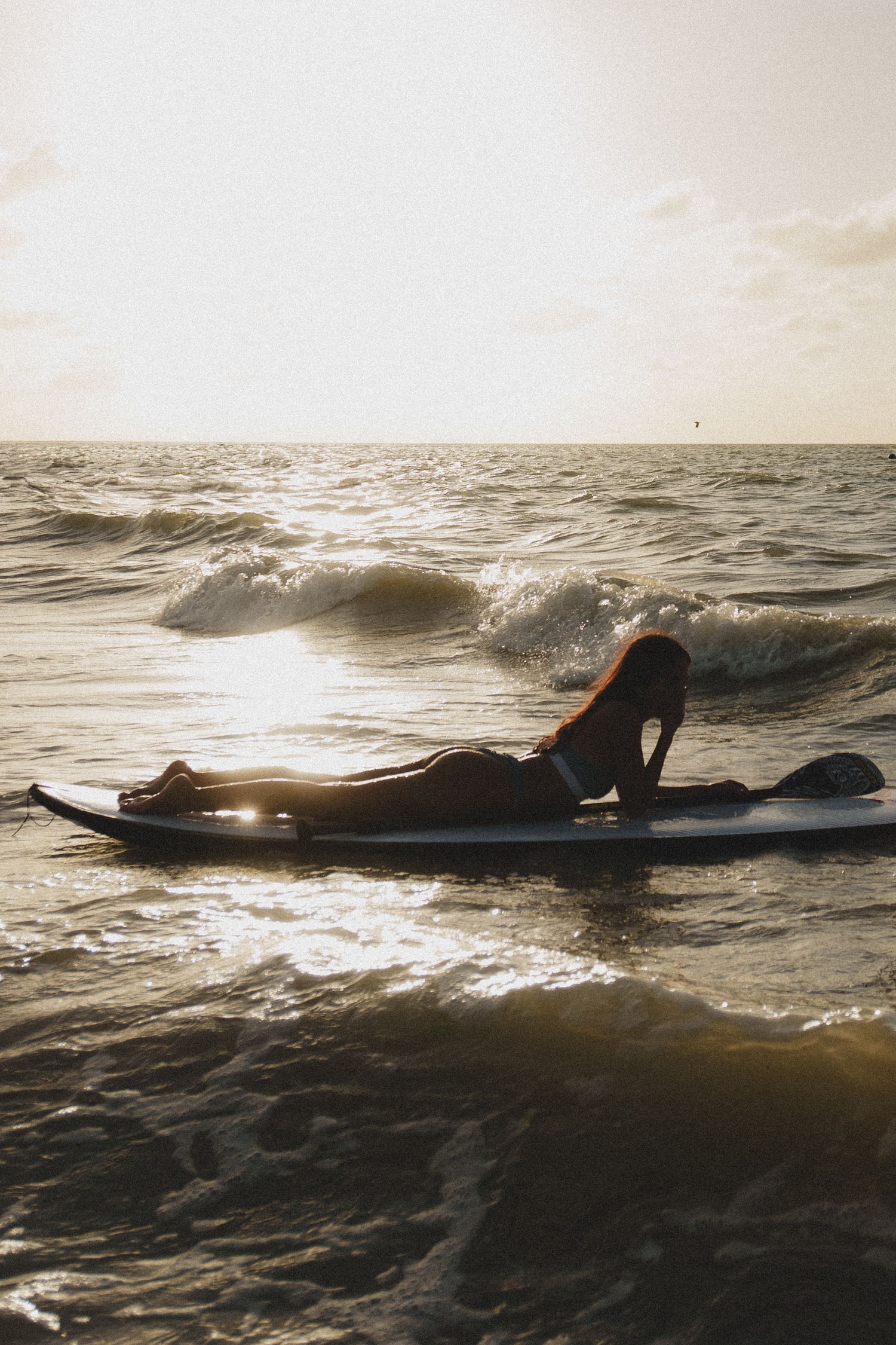 Silhouette of a surfer riding waves during a dramatic ocean sunset with golden light reflecting off the water.