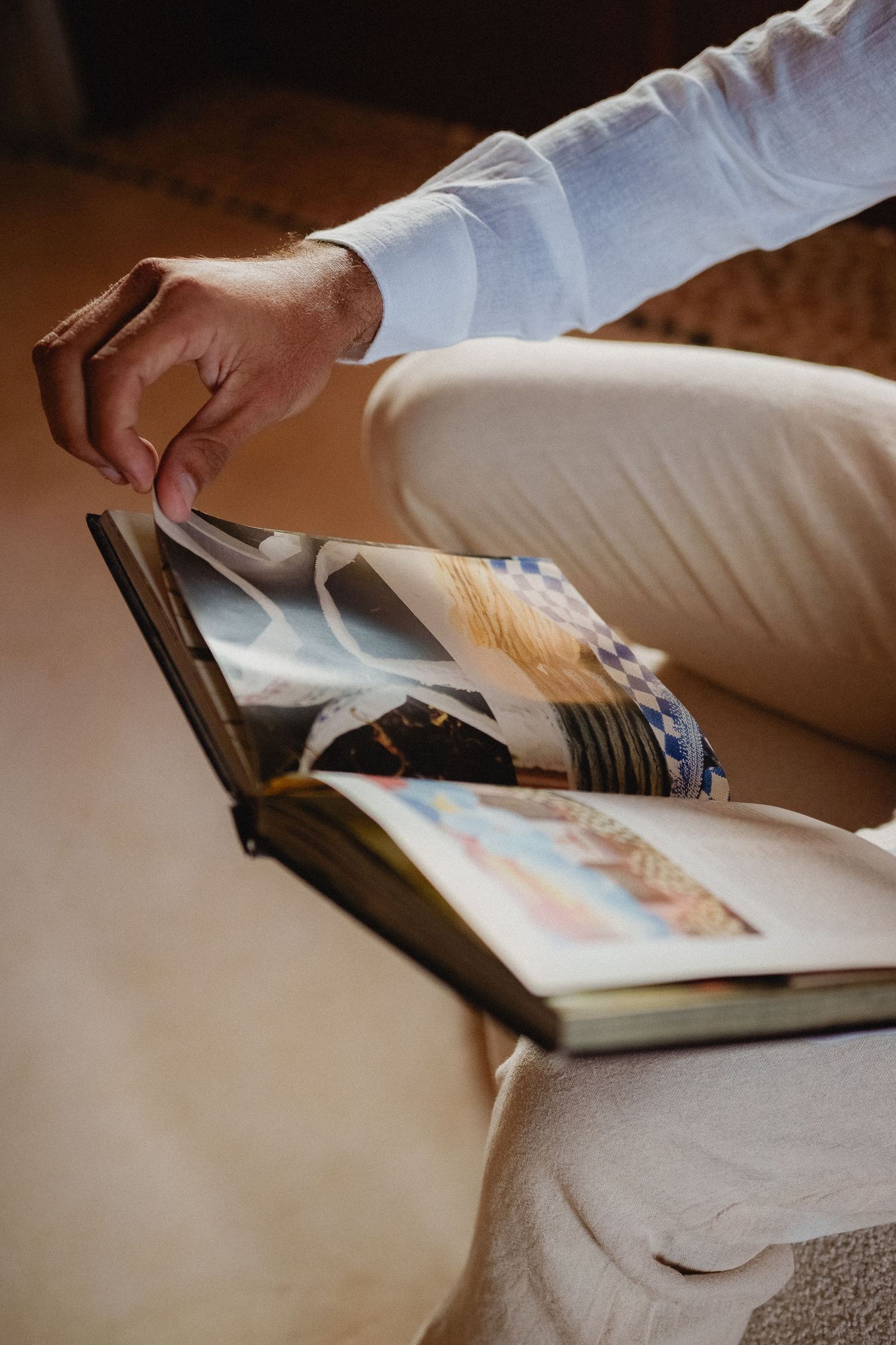 Close-up view of hands flipping through pages of an open book on a textured surface in warm lighting.