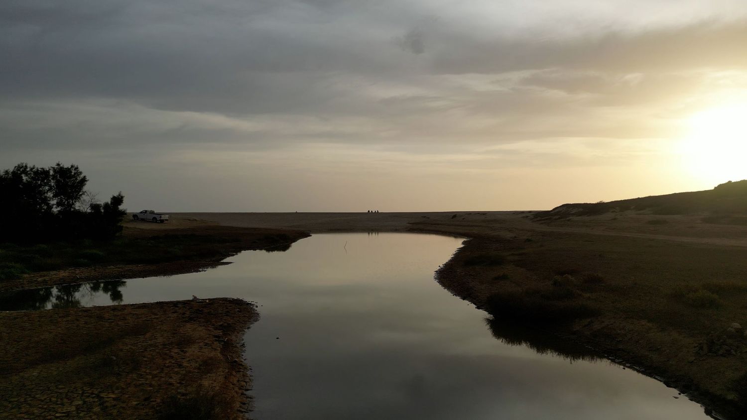 A panoramic view of a serene lake at sunset with misty clouds reflecting on the calm water surface.