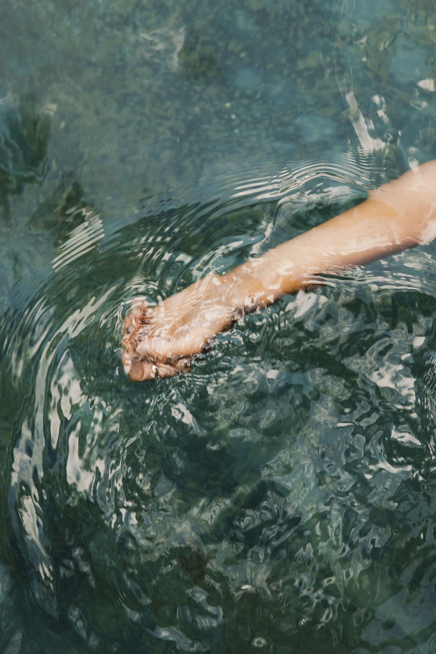 Hand creating ripples in clear blue pool water with artistic motion effect.