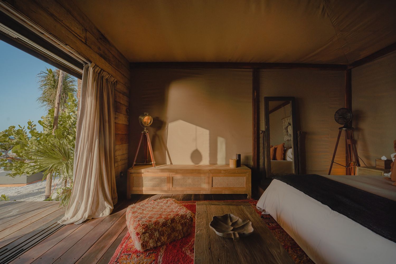 Interior view of a cozy glamping tent with natural light streaming through windows and draped fabric.