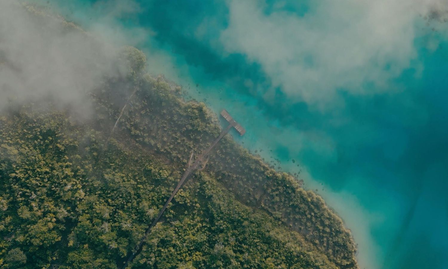 Aerial view of a lush green mountainous coastline with turquoise ocean waters and dramatic cliffs in the tropics.