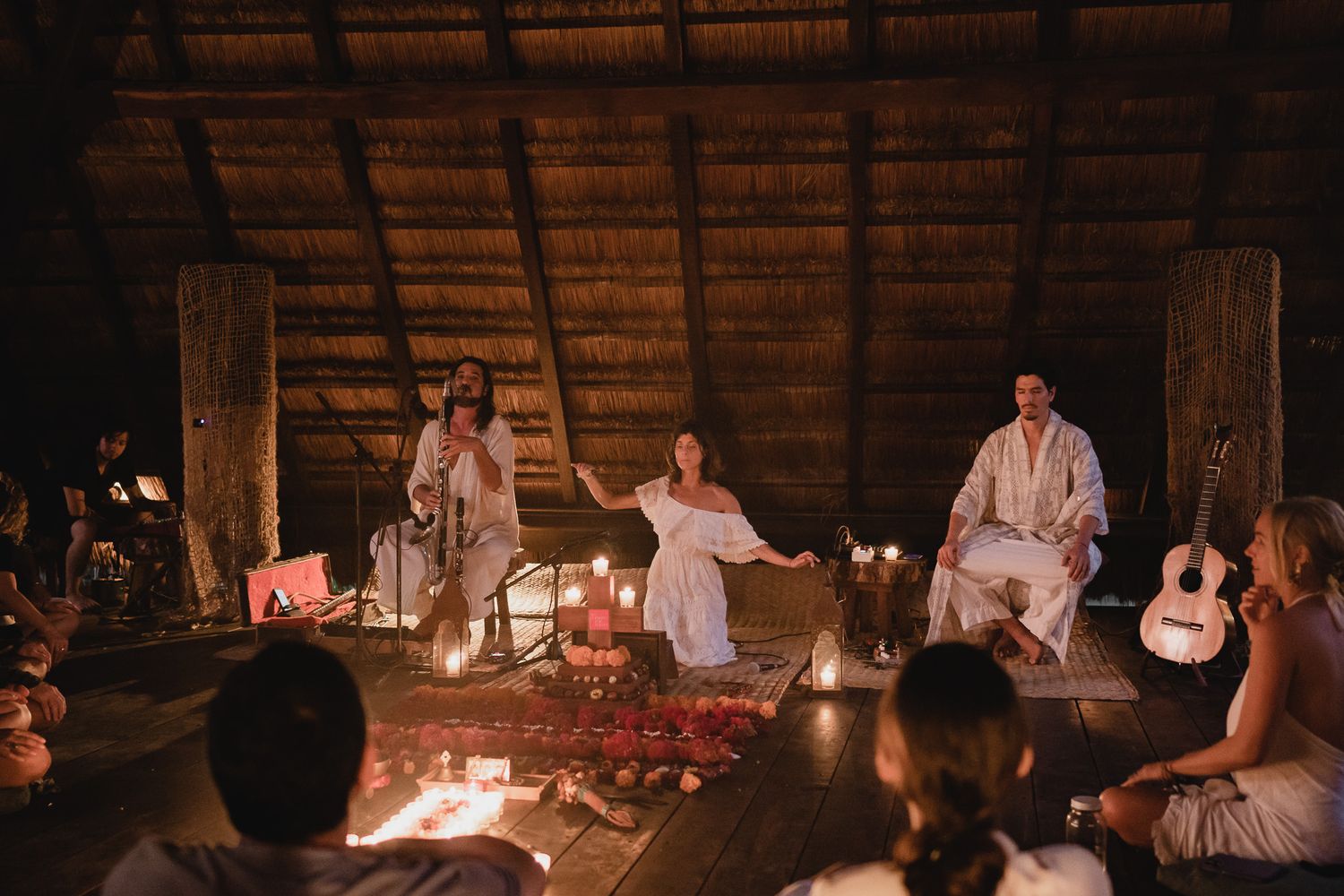 A traditional thatched-roof gathering space lit by warm candlelight during an evening event.