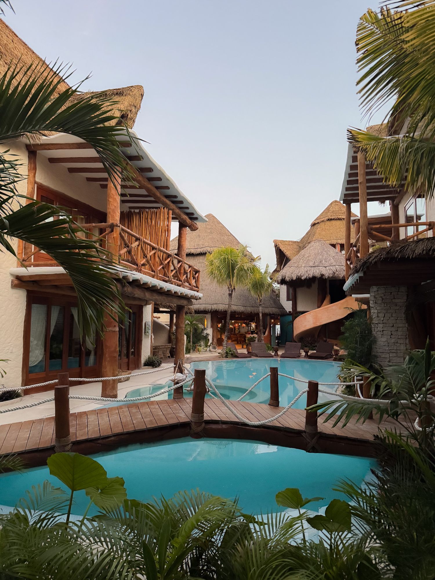 Tropical resort with thatched-roof bungalows and swimming pool surrounded by palm trees.