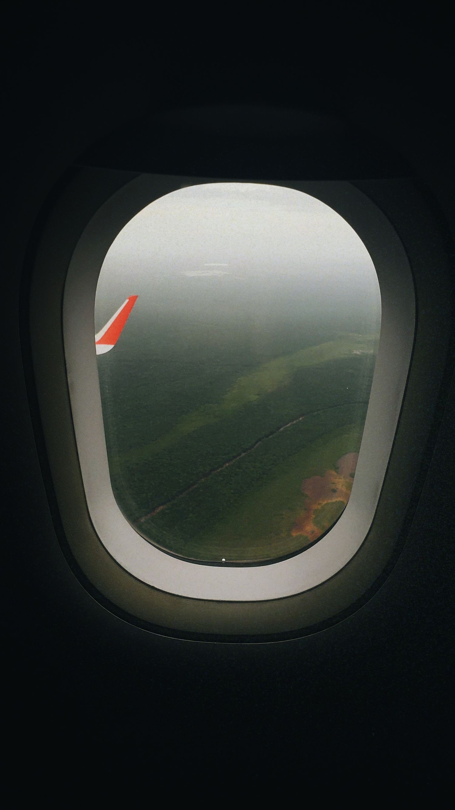 View of green landscape and wing tip through airplane window during flight.