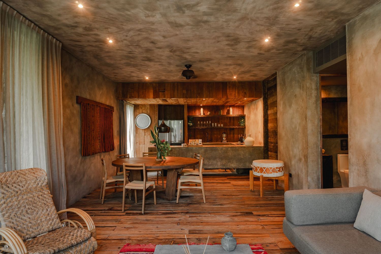 Modern industrial-style loft interior with concrete walls, recessed lighting, and rustic wooden furniture.