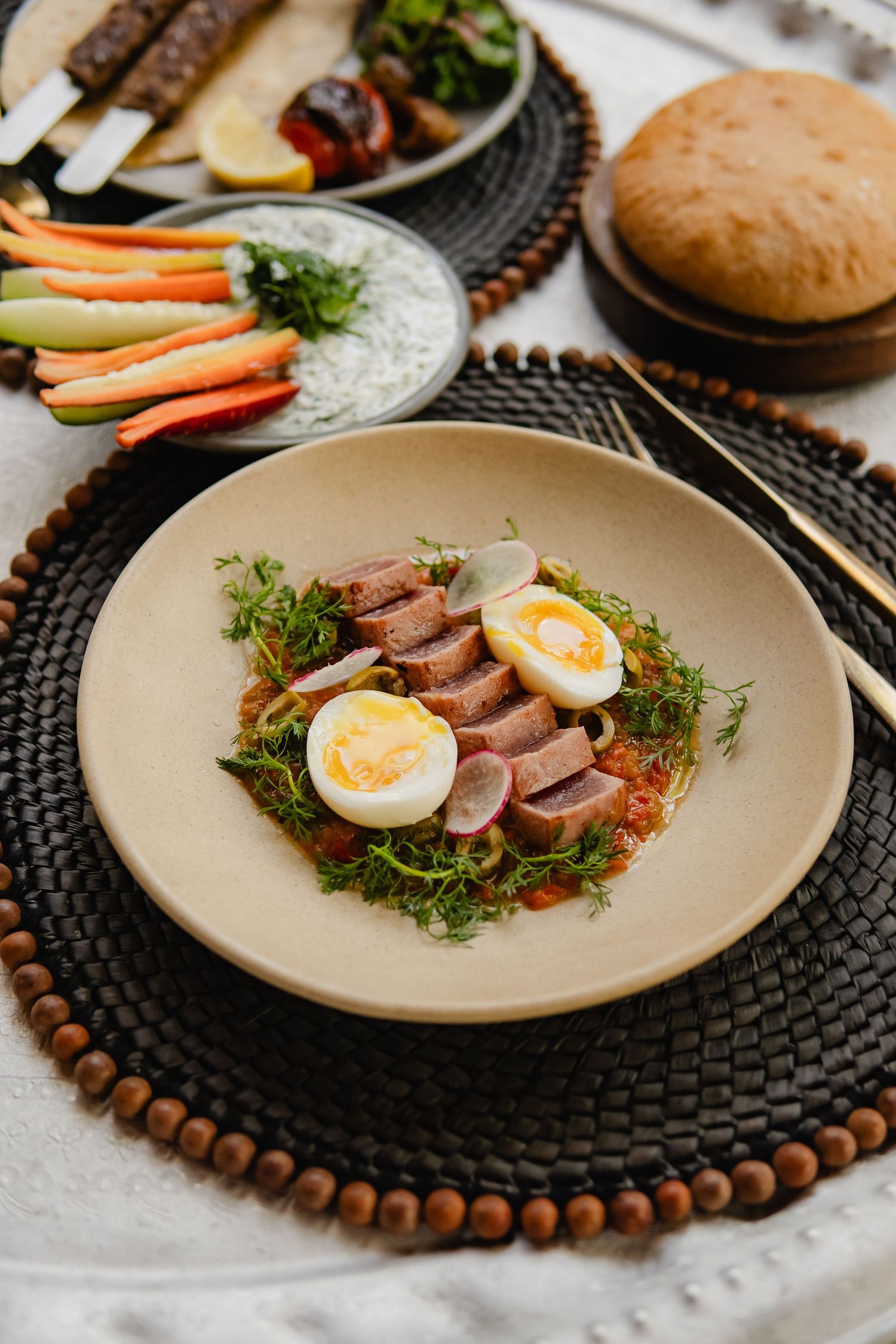 Elegant plated dish with sliced meat, boiled egg, and fresh herbs on a wooden beaded placemat.