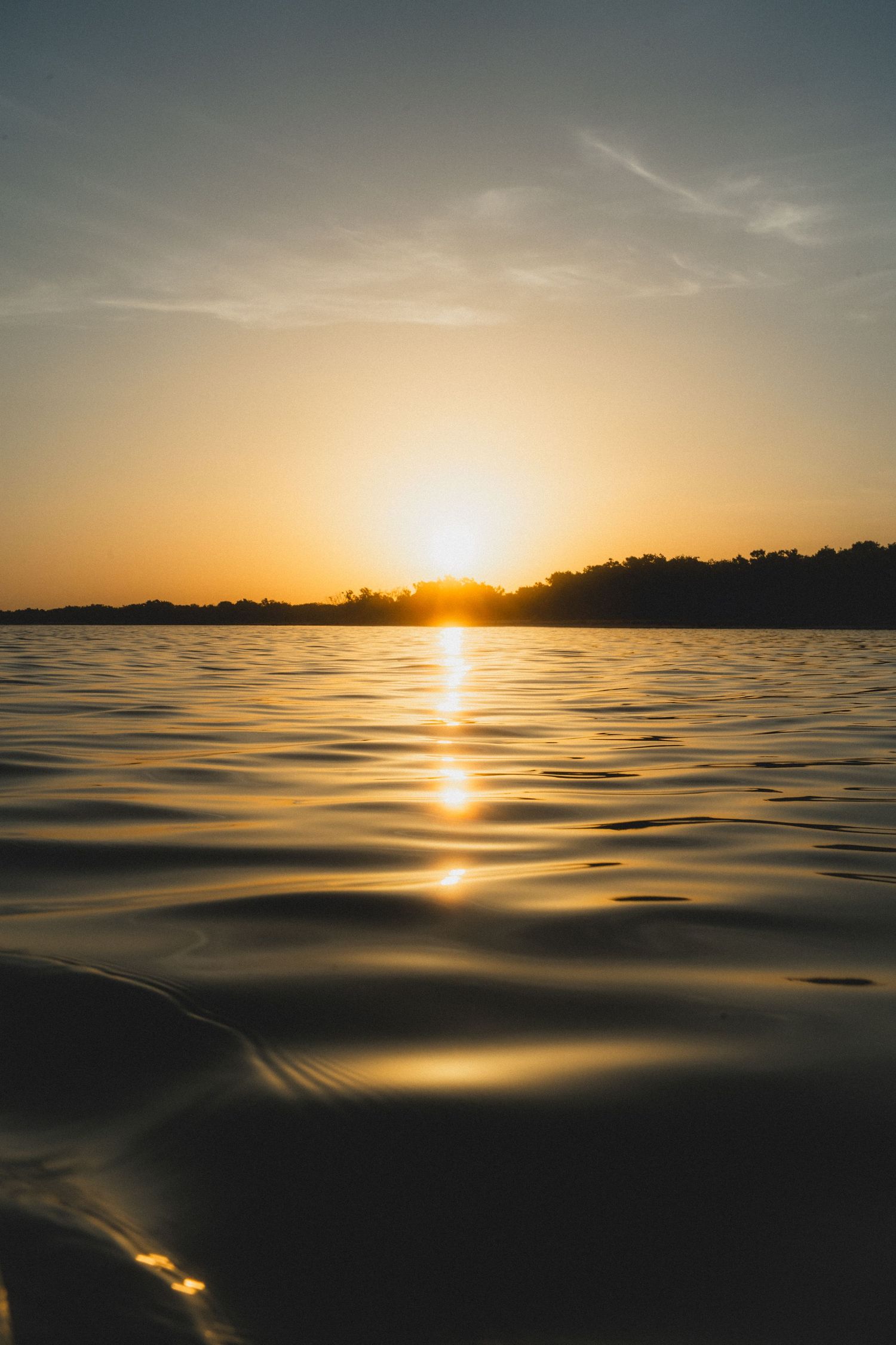 Tranquil sunset over calm ocean waters with golden sunlight reflecting off gentle rippling waves at dusk.