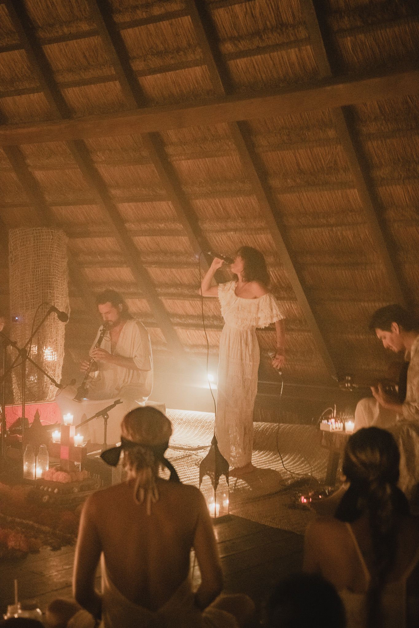 A series of dimly lit concert photos showing silhouettes of performers on stage under a rustic thatched roof venue.