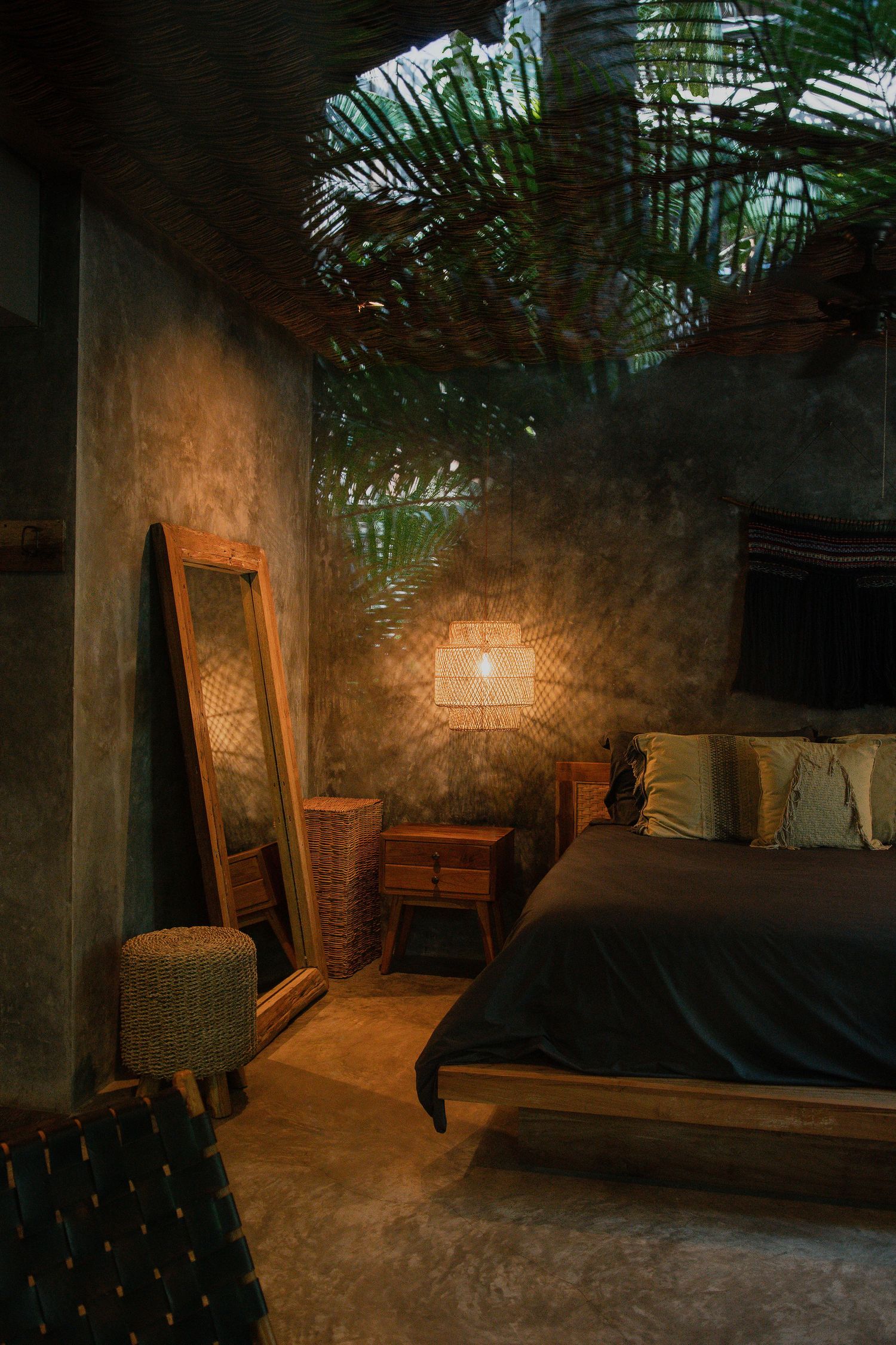 Dimly lit interior space with exposed brick walls, wooden furniture and palm fronds creating a moody atmosphere.