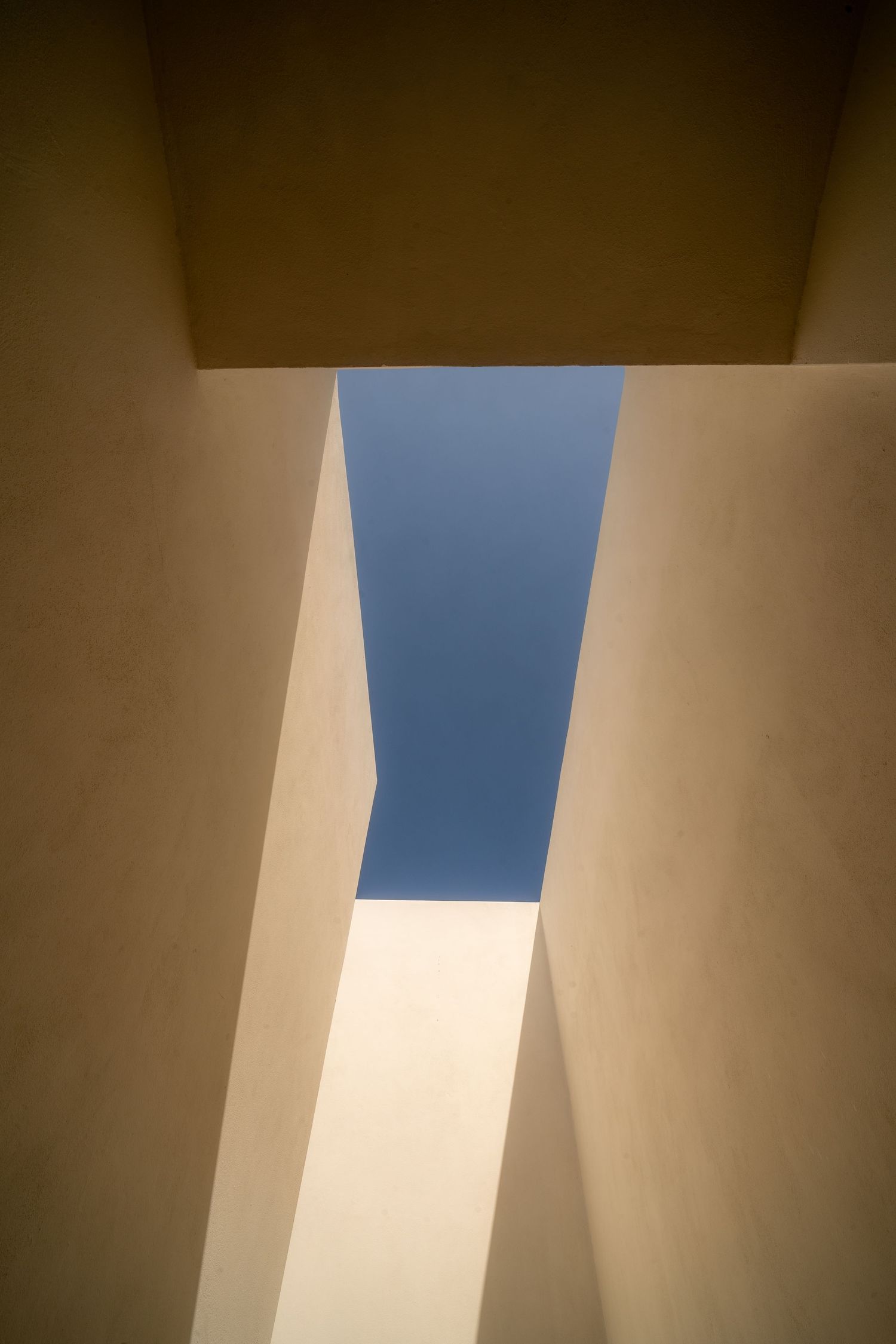 Abstract architectural photography showing geometric shapes and shadows with blue sky visible through skylight.