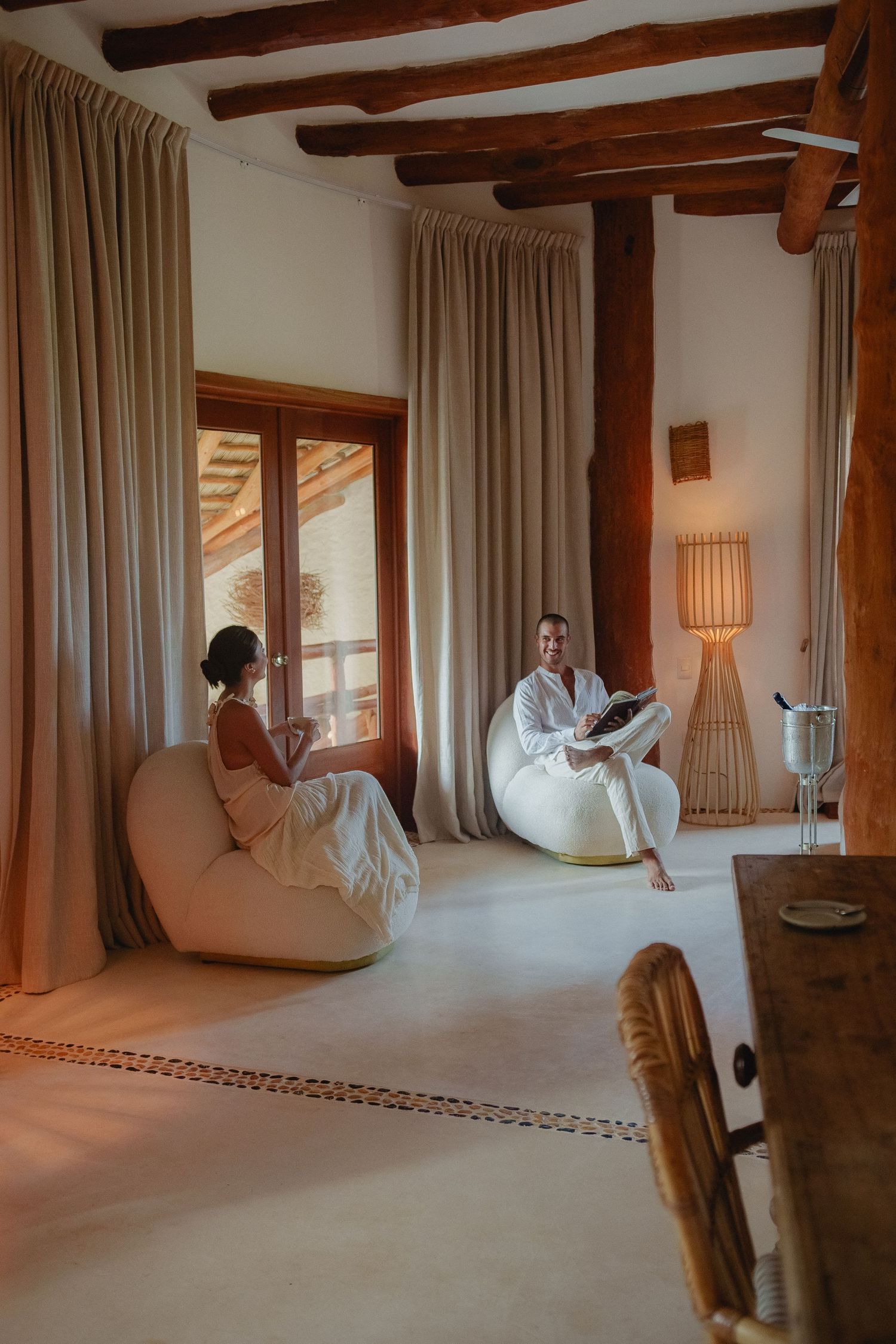Rustic bedroom interior with exposed wooden beams, flowing curtains, and soft natural lighting creating a cozy atmosphere.
