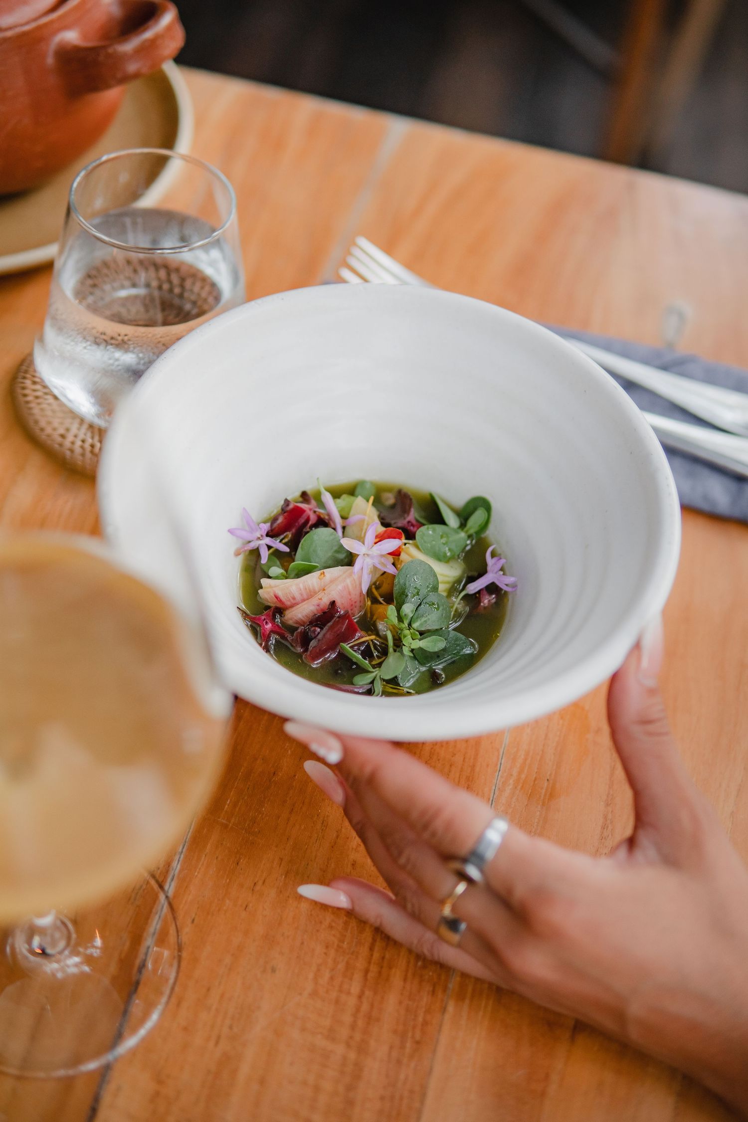 A white ceramic bowl of fresh salad with edible flowers being served on a wooden table.