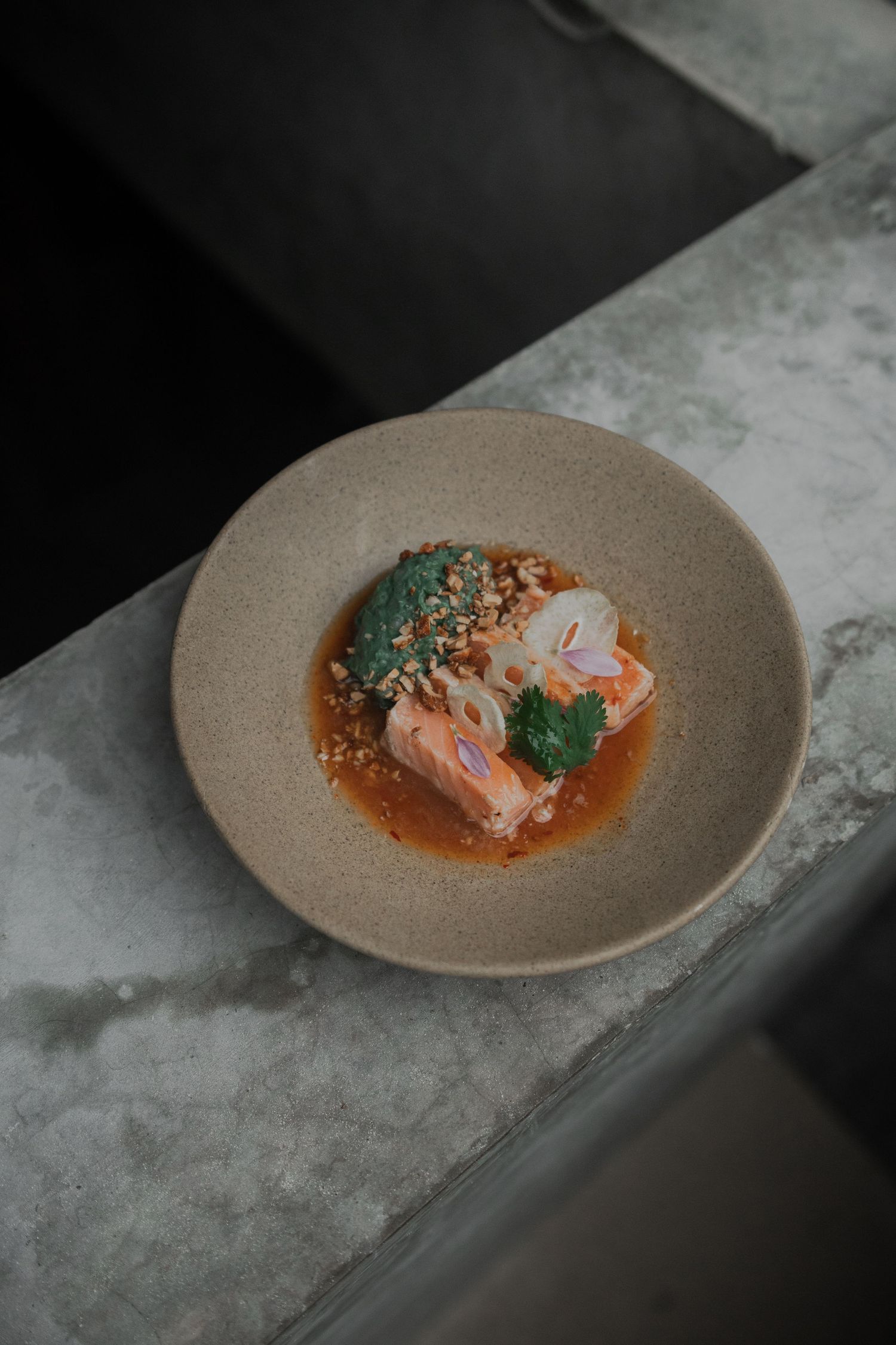 Artfully plated salmon dish with vibrant red sauce and delicate herbs served on a textured beige ceramic plate.