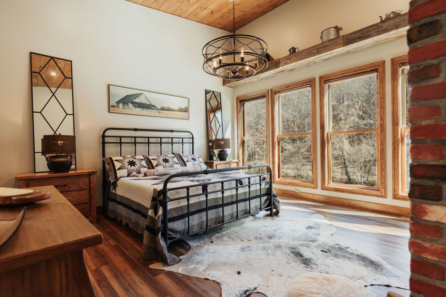 A bed with a cowskin rug at the base of it and large windows on the right.