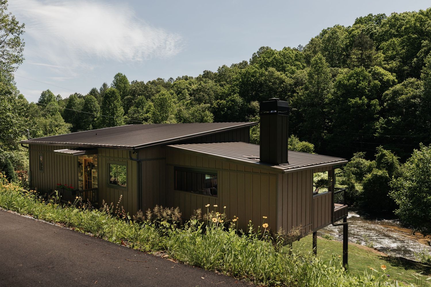 A brown cabin rests on stilts overlooking the river below, surrounded by trees.