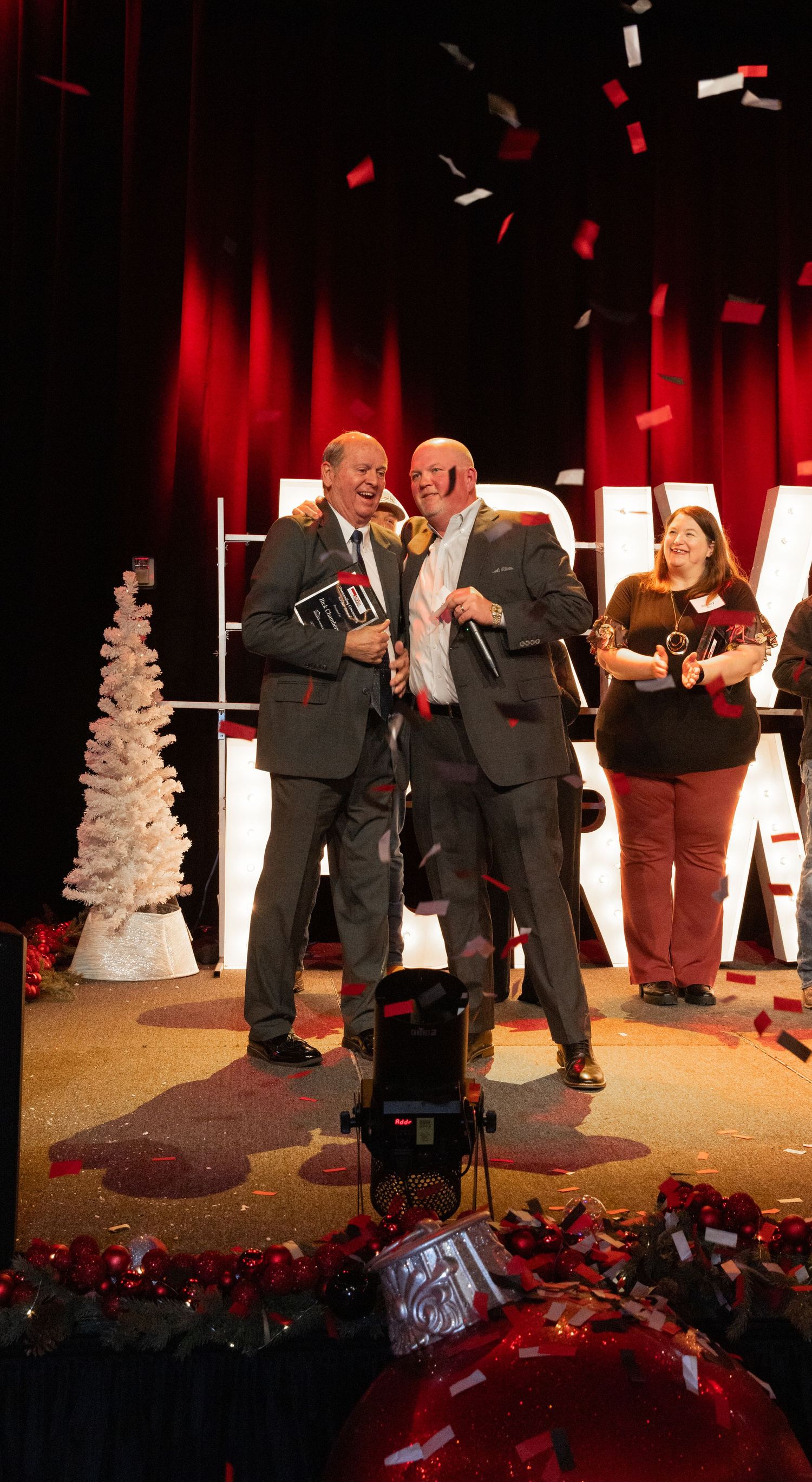 Two men warmly shake hands as confetti falls.