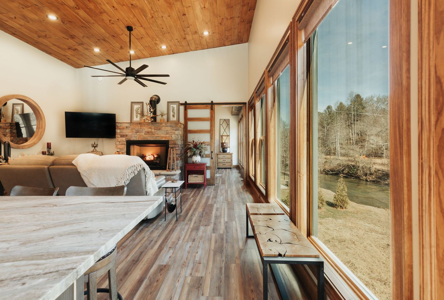 Large windows showing a river on the left, and a fireplace in the far back of the room is lit.