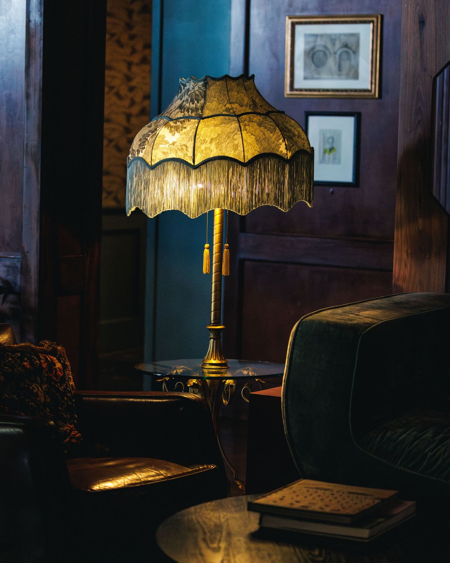 green lamp with fringes and a glass table base is surrounded by a leather chair on the left and a velvet couch on the right