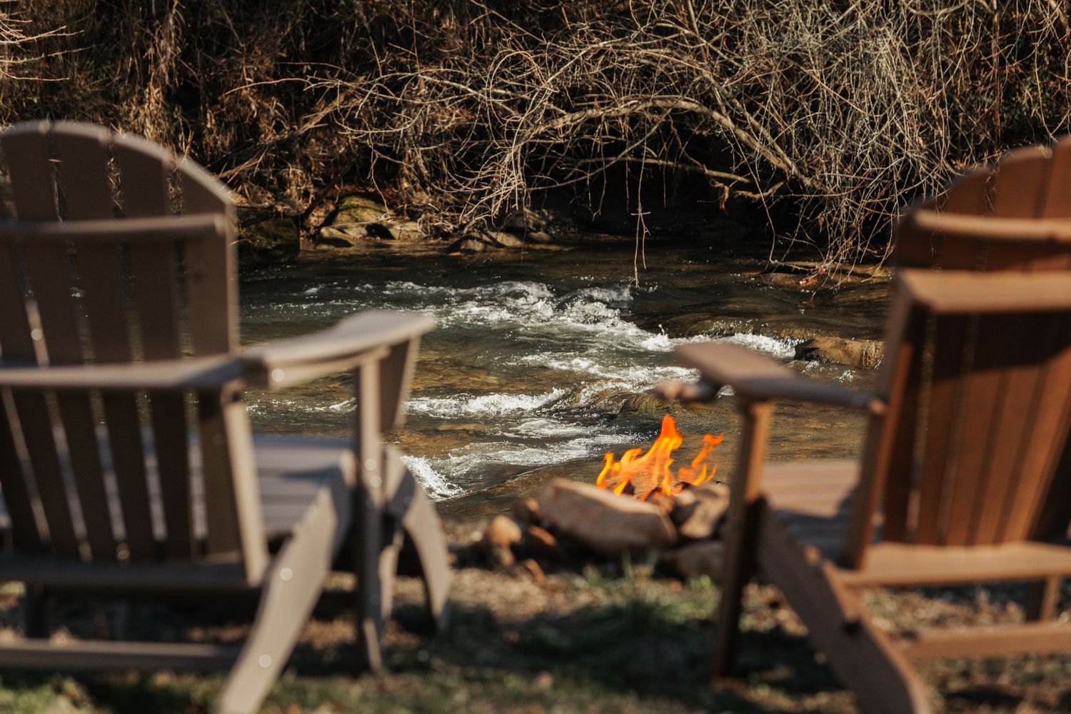 Two chairs overlook a campfire with a roaring river behind it.