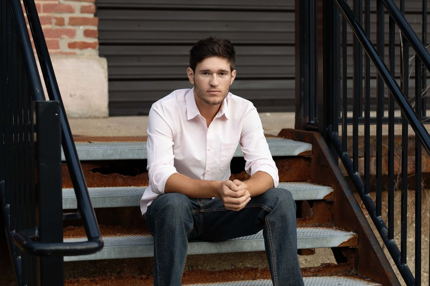 A person in casual attire sits on outdoor steps while looking at their mobile phone.