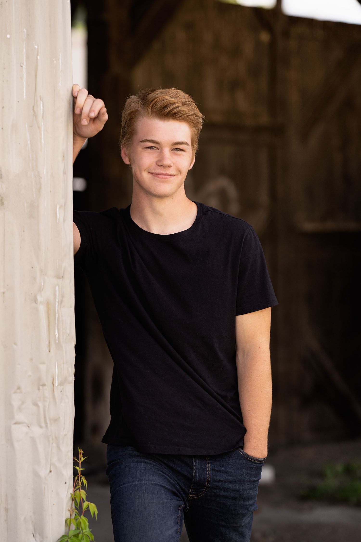Casual portrait leaning against white wall in black t-shirt and jeans.