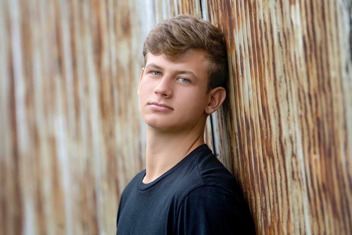 Natural light portrait against rustic wooden wall background in casual setting.