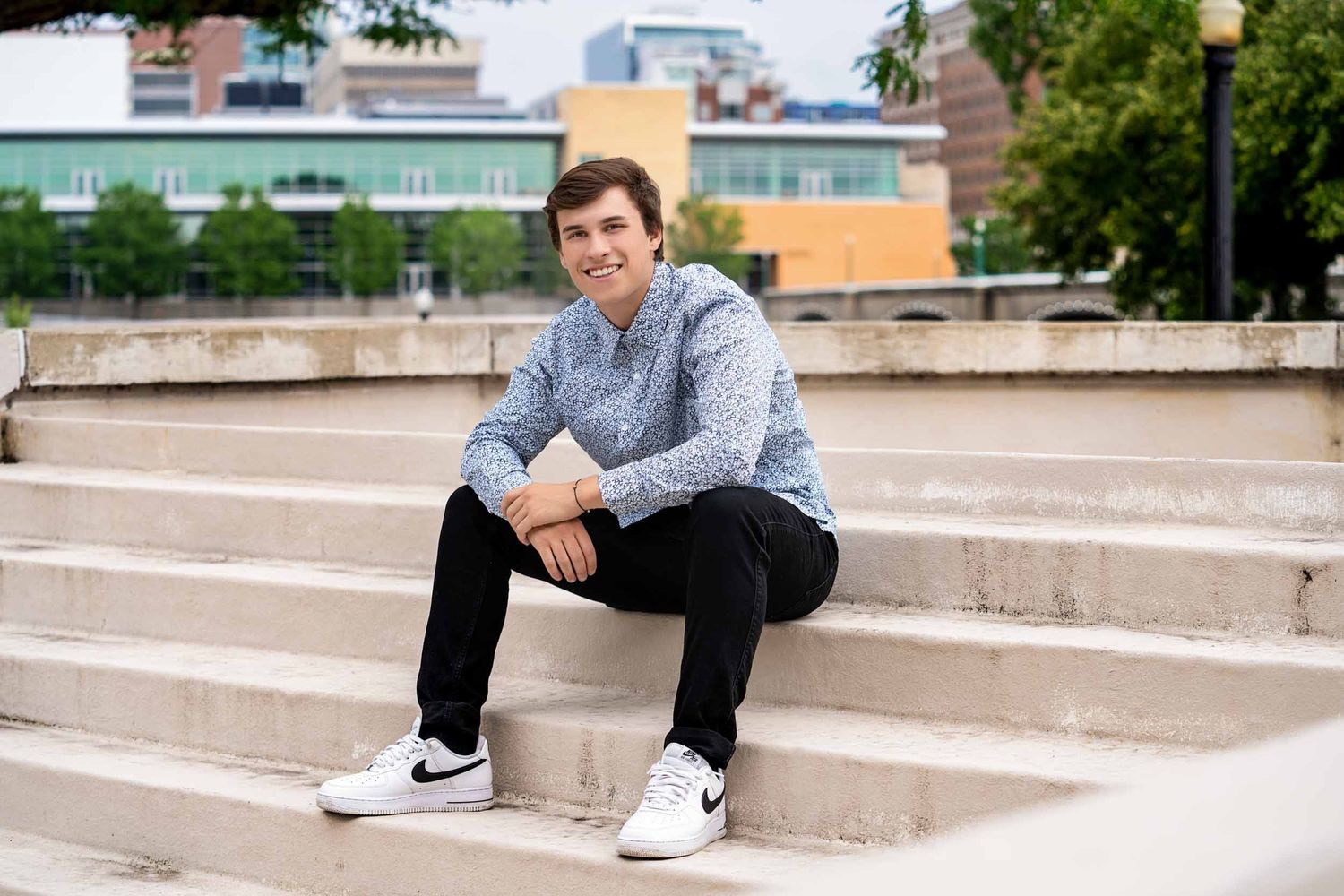 A person sits casually on concrete steps wearing a blue sweater and black pants with Nike sneakers.