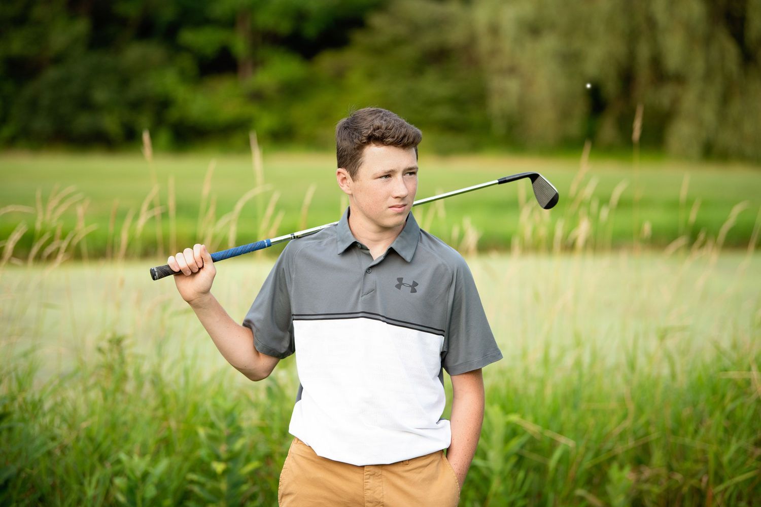 Golfer in polo shirt holds club over shoulder while standing in grassy field.