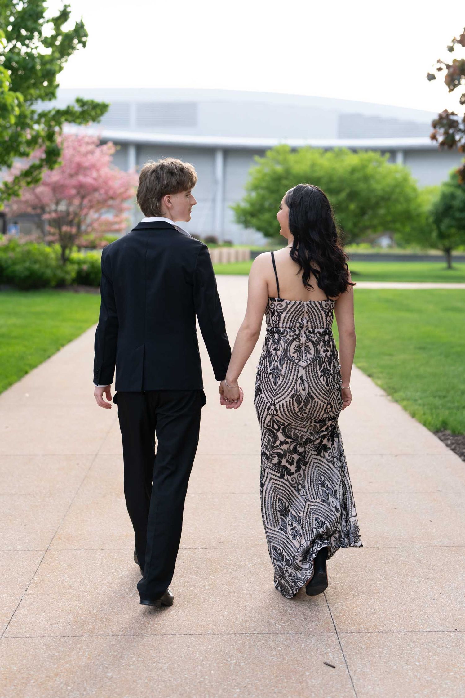 A couple in formal attire walking hand in hand down a concrete path, shown in a series of similar shots.