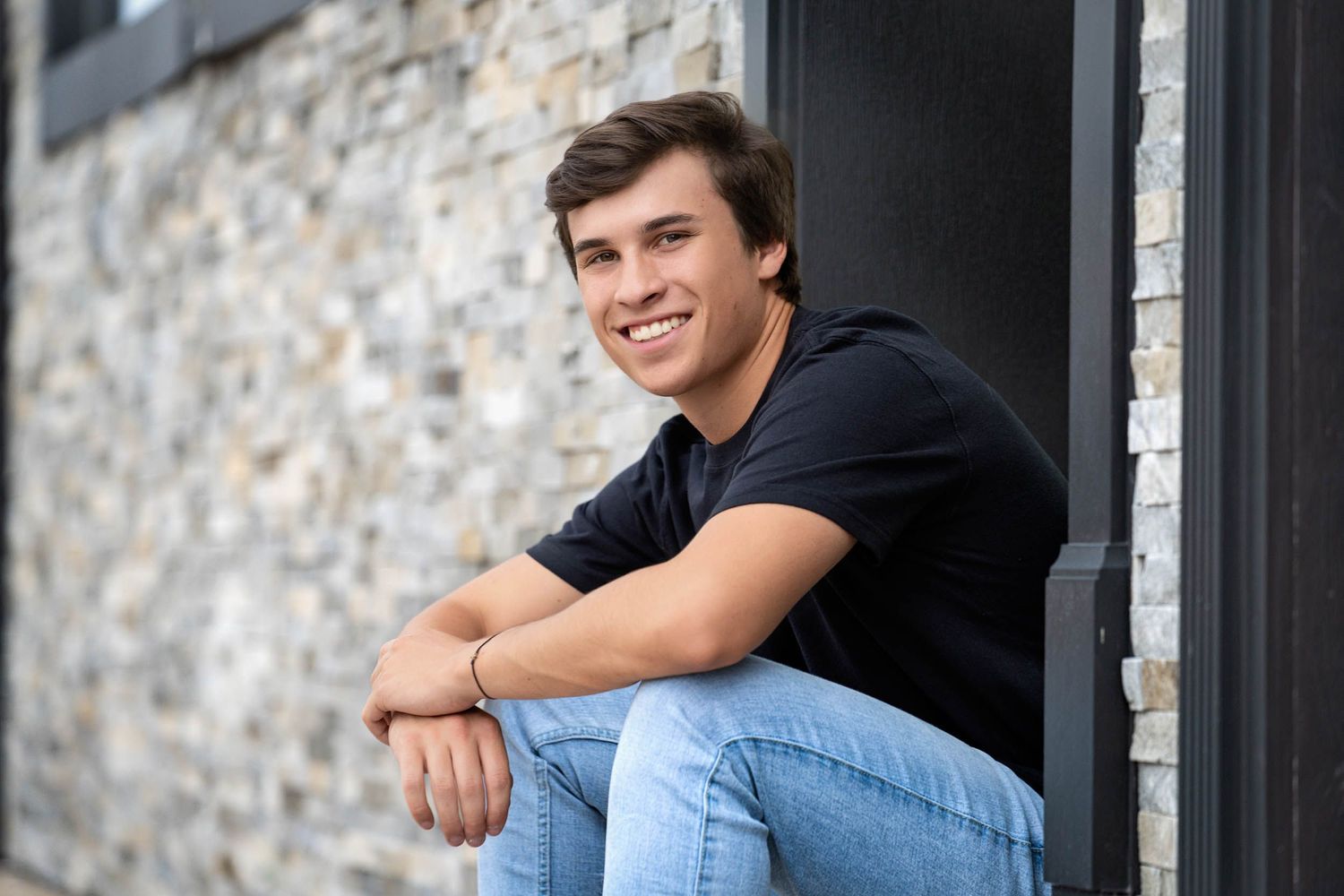 Young person in casual attire sitting on outdoor steps by a brick wall smiling at the camera.