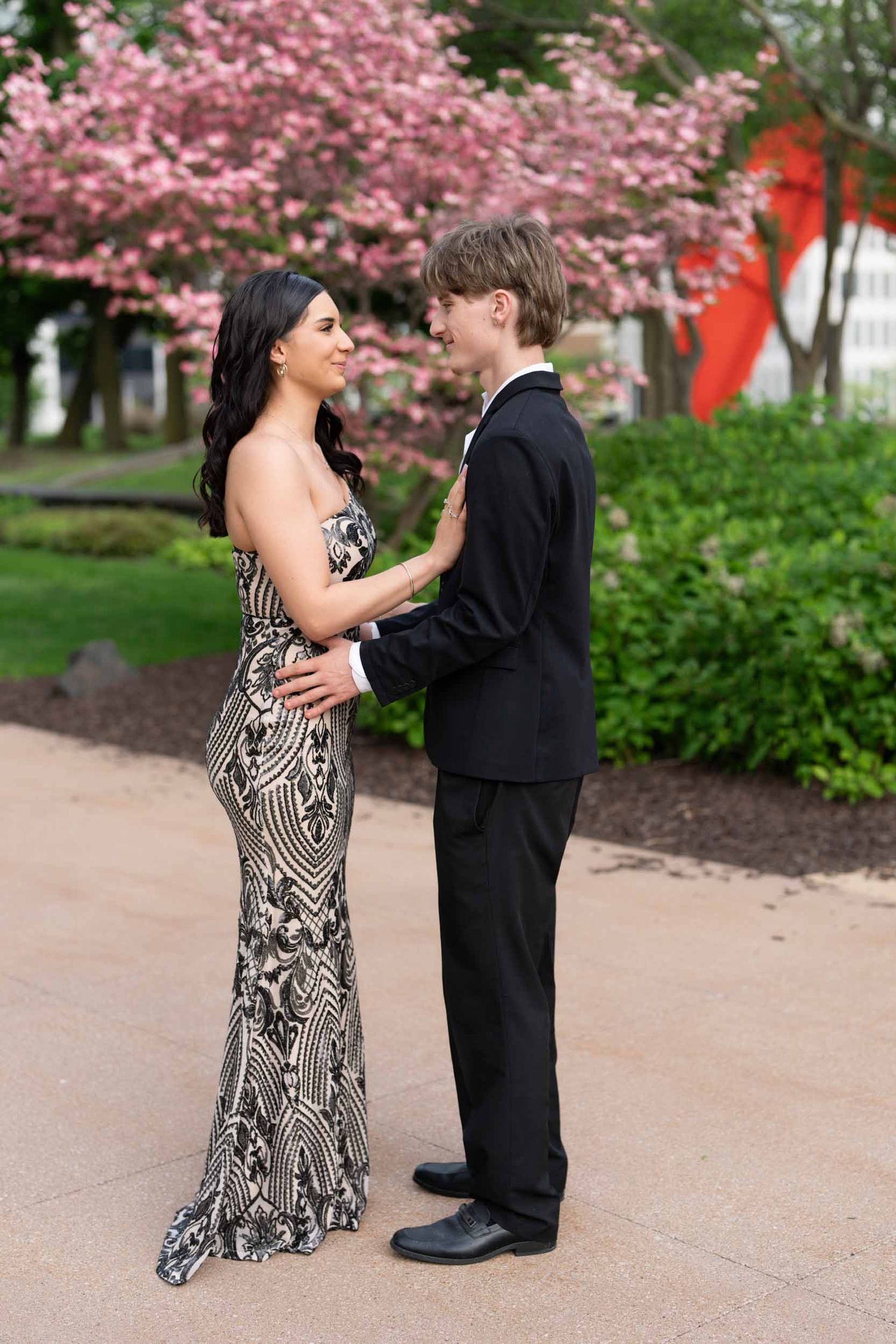 Mother and young son in formal attire embrace during graduation celebration with pink cherry blossoms.