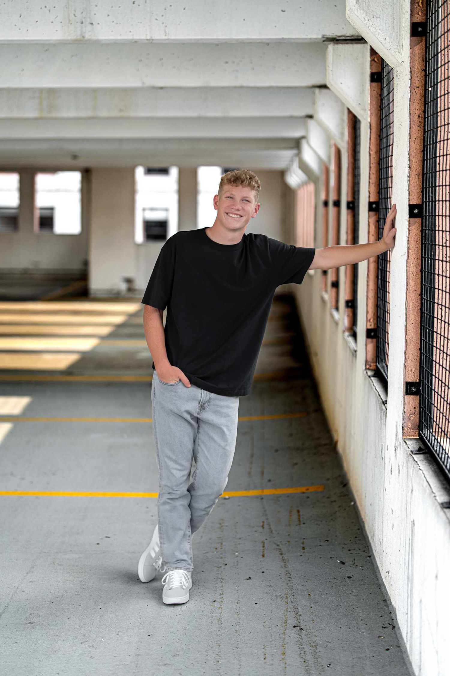 Casual fashion poses in a parking garage wearing black t-shirt and gray pants.
