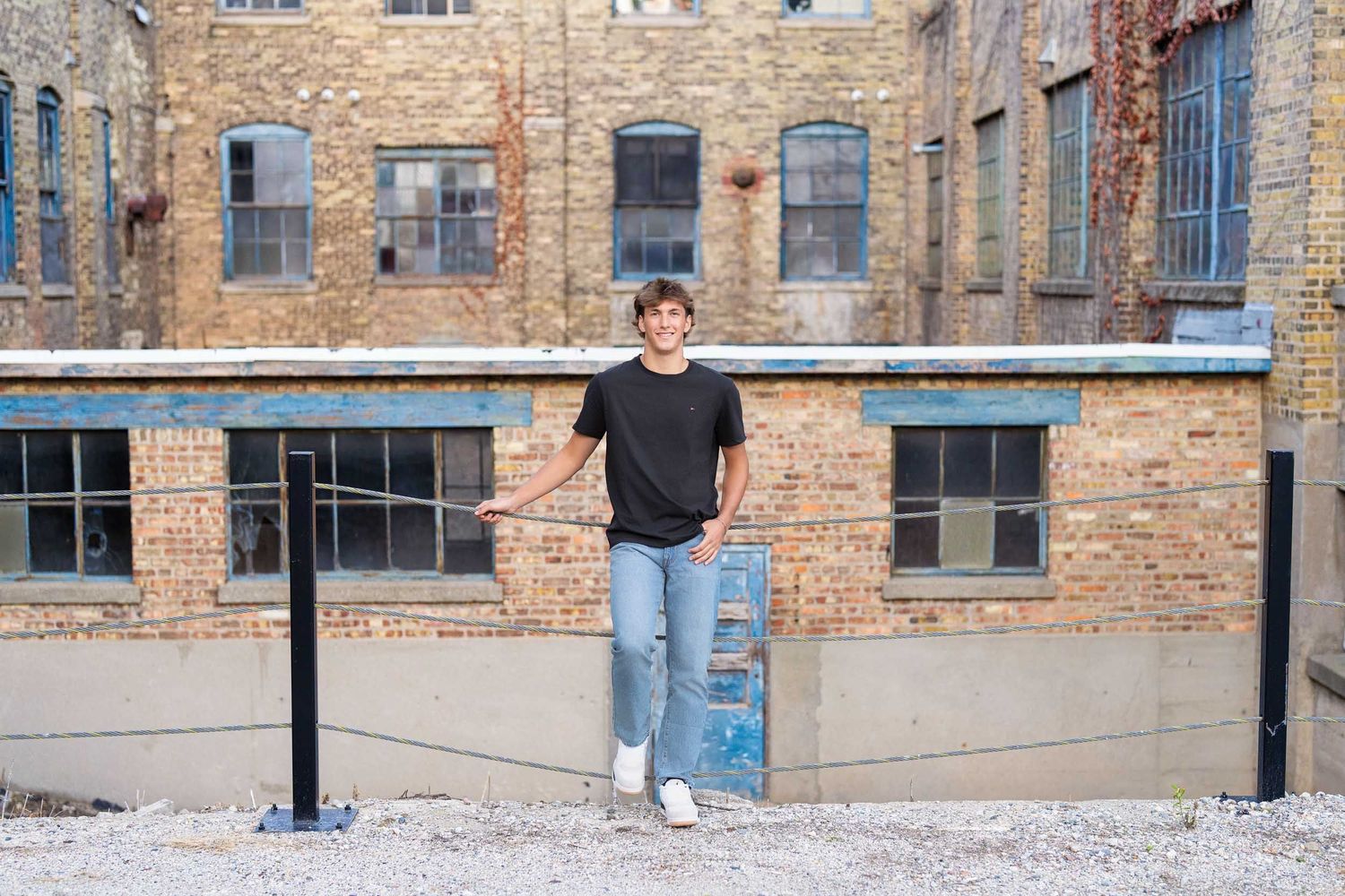 Casual portrait against rustic brick building with industrial windows and metal railing.