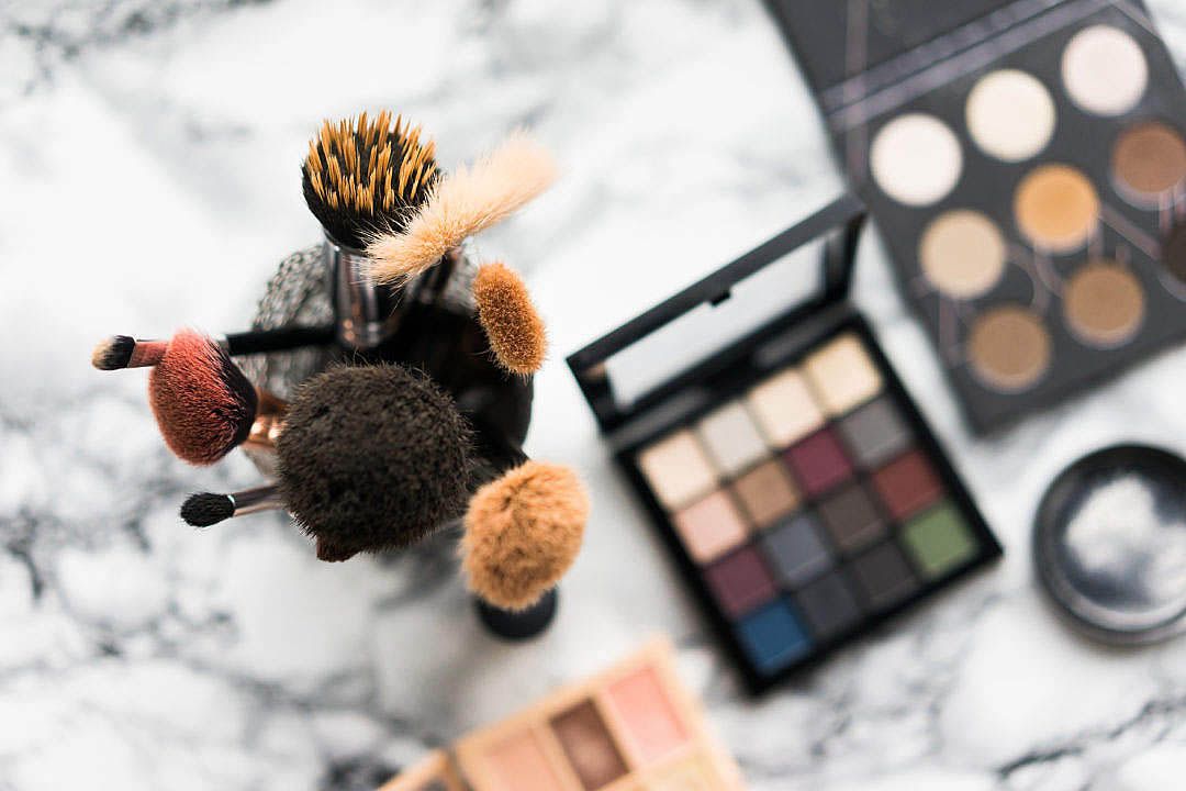 Makeup brushes and cosmetic palettes arranged on marble background.