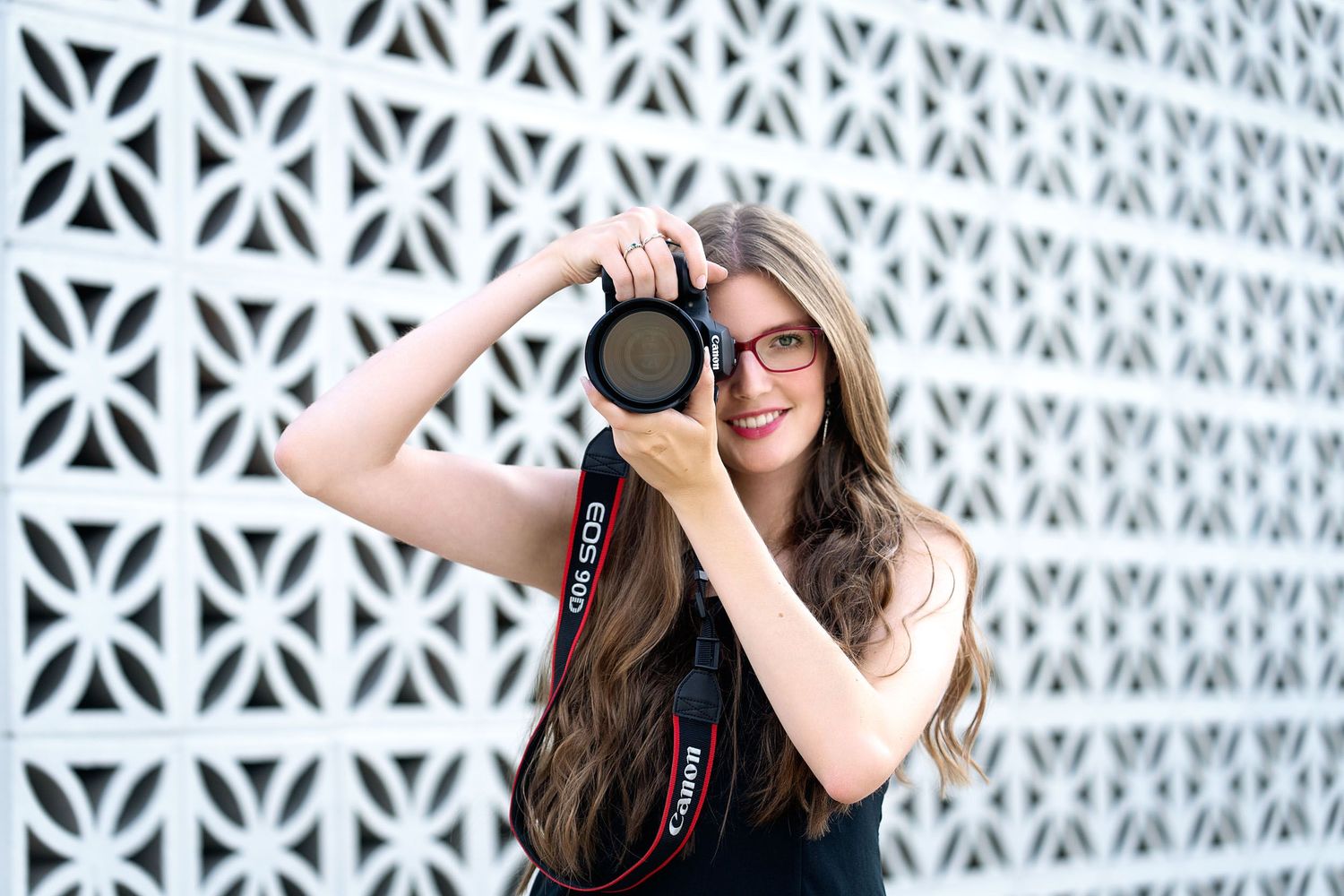 A photographer holds up a camera against a geometric patterned wall background.