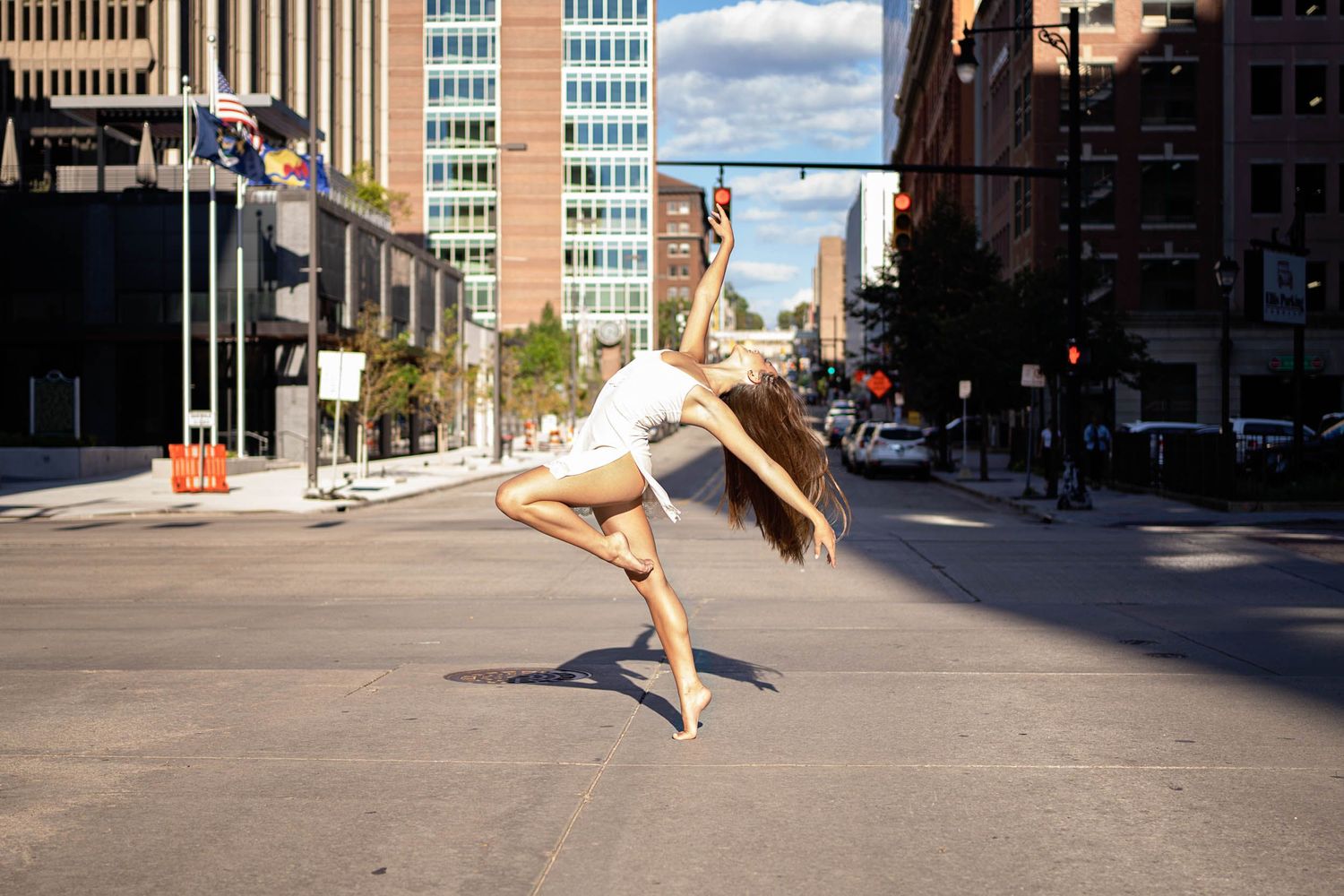 A dancer leaps gracefully in an urban street setting between tall buildings.
