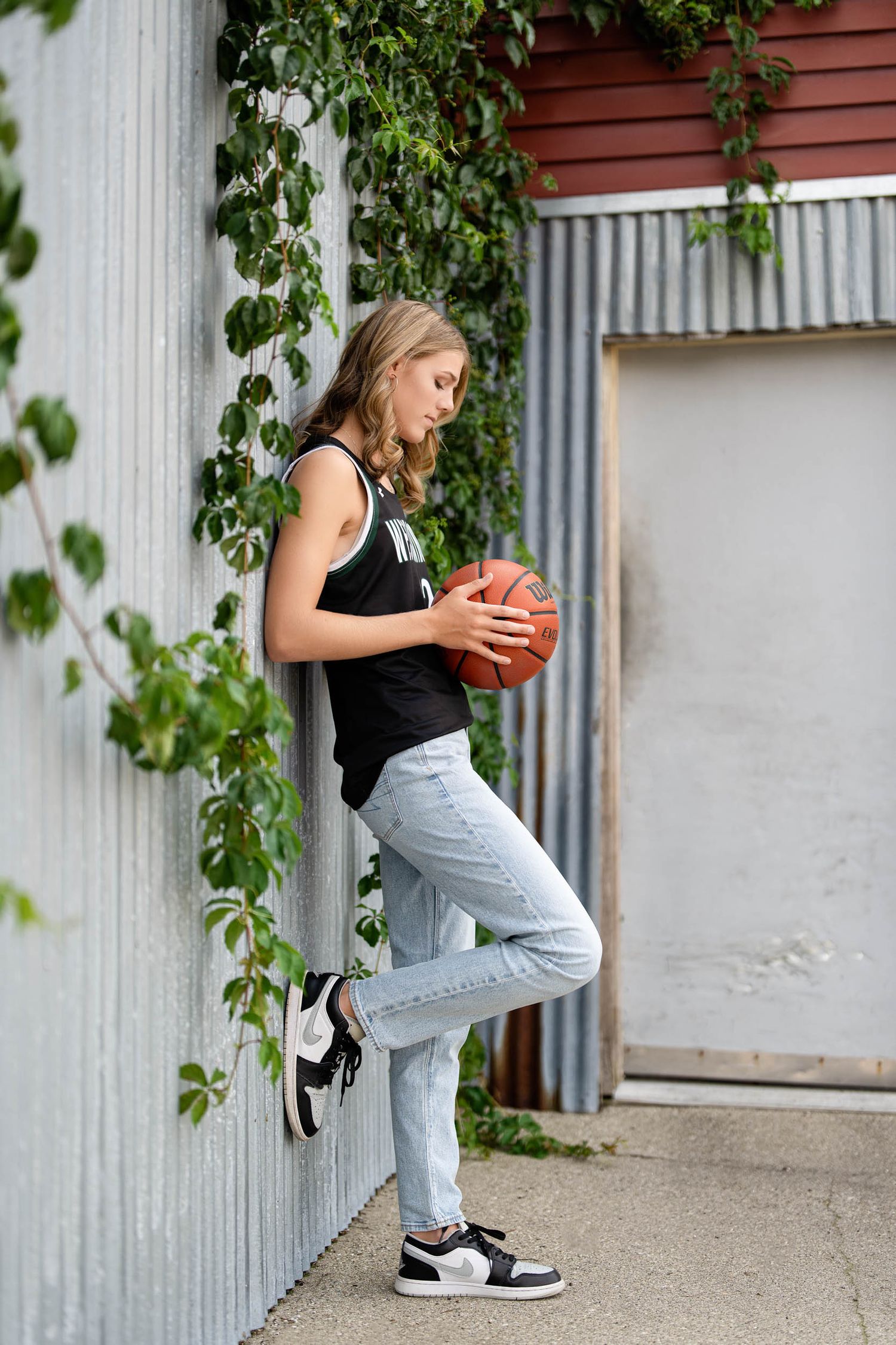 Basketball player practicing dribbling moves against an industrial backdrop with red wall.