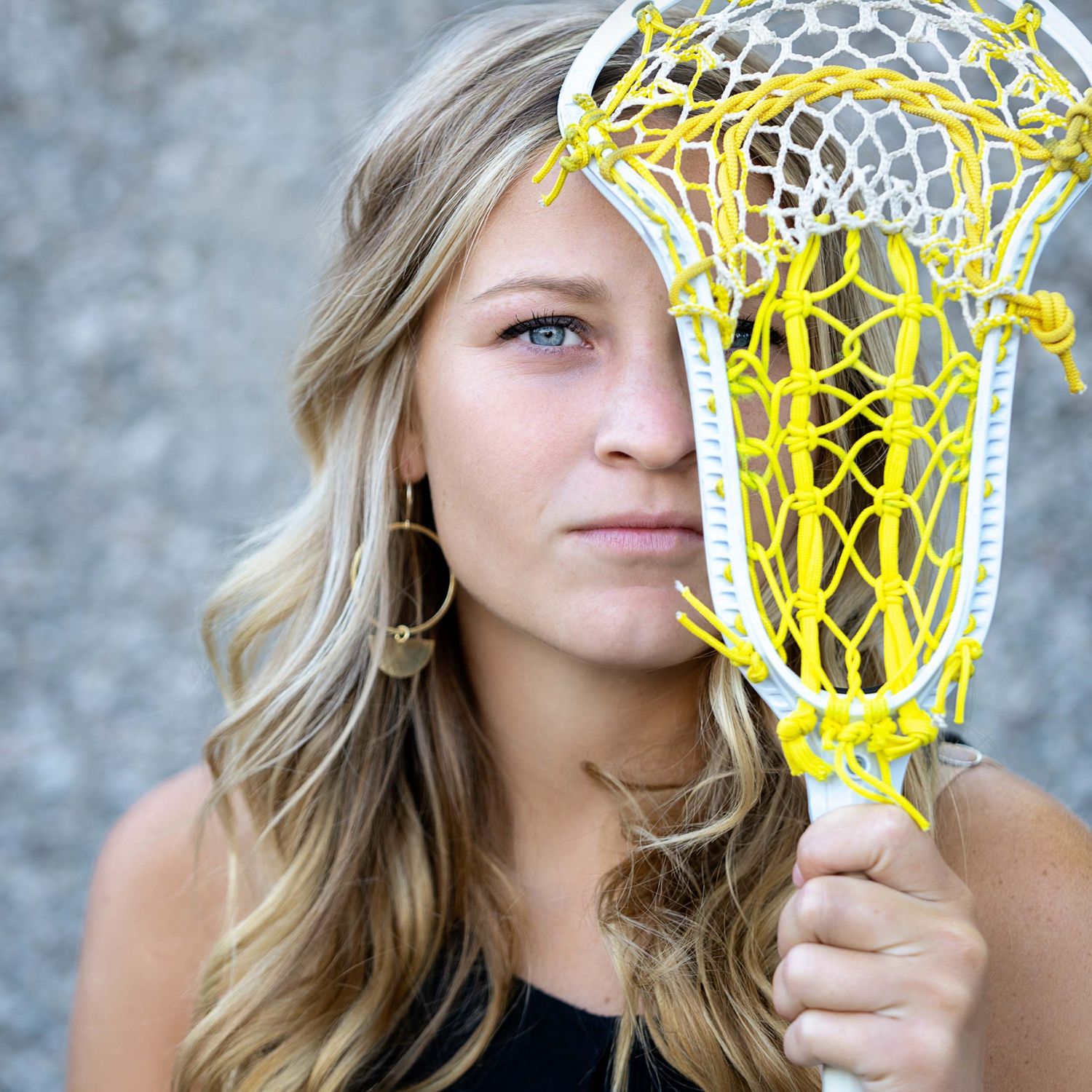 A yellow lacrosse stick held up against a gray background.