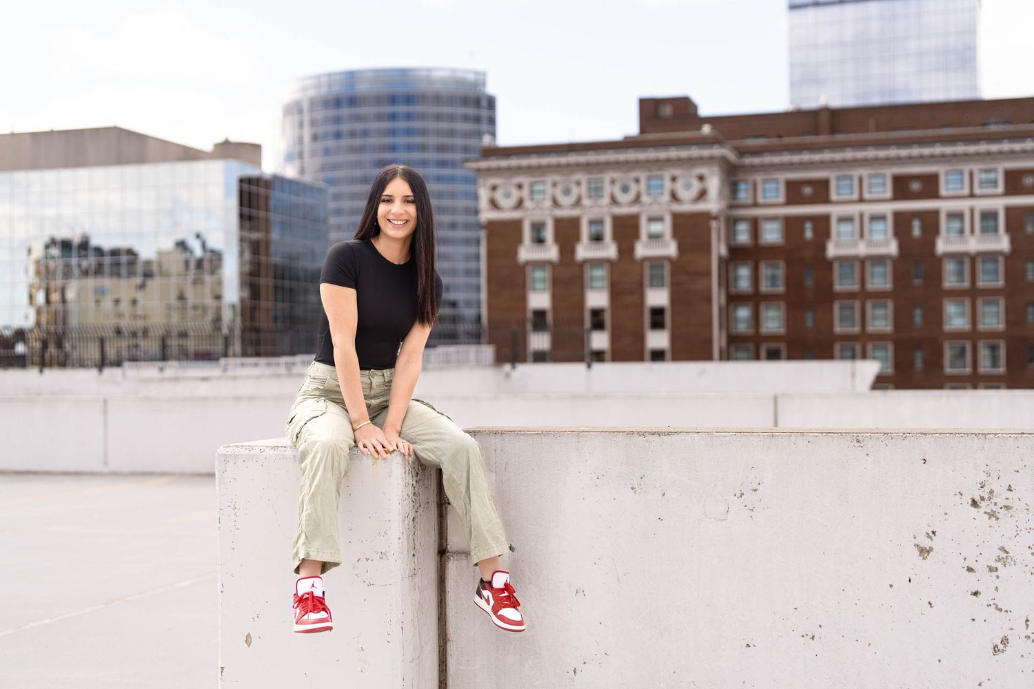 A person in casual attire sits on a concrete ledge of an urban rooftop with city buildings in the background.