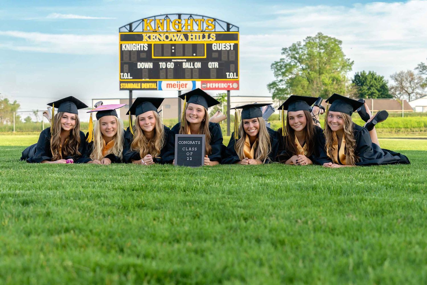 Graduates in black caps and gowns pose together on a grassy hill during commencement ceremonies.