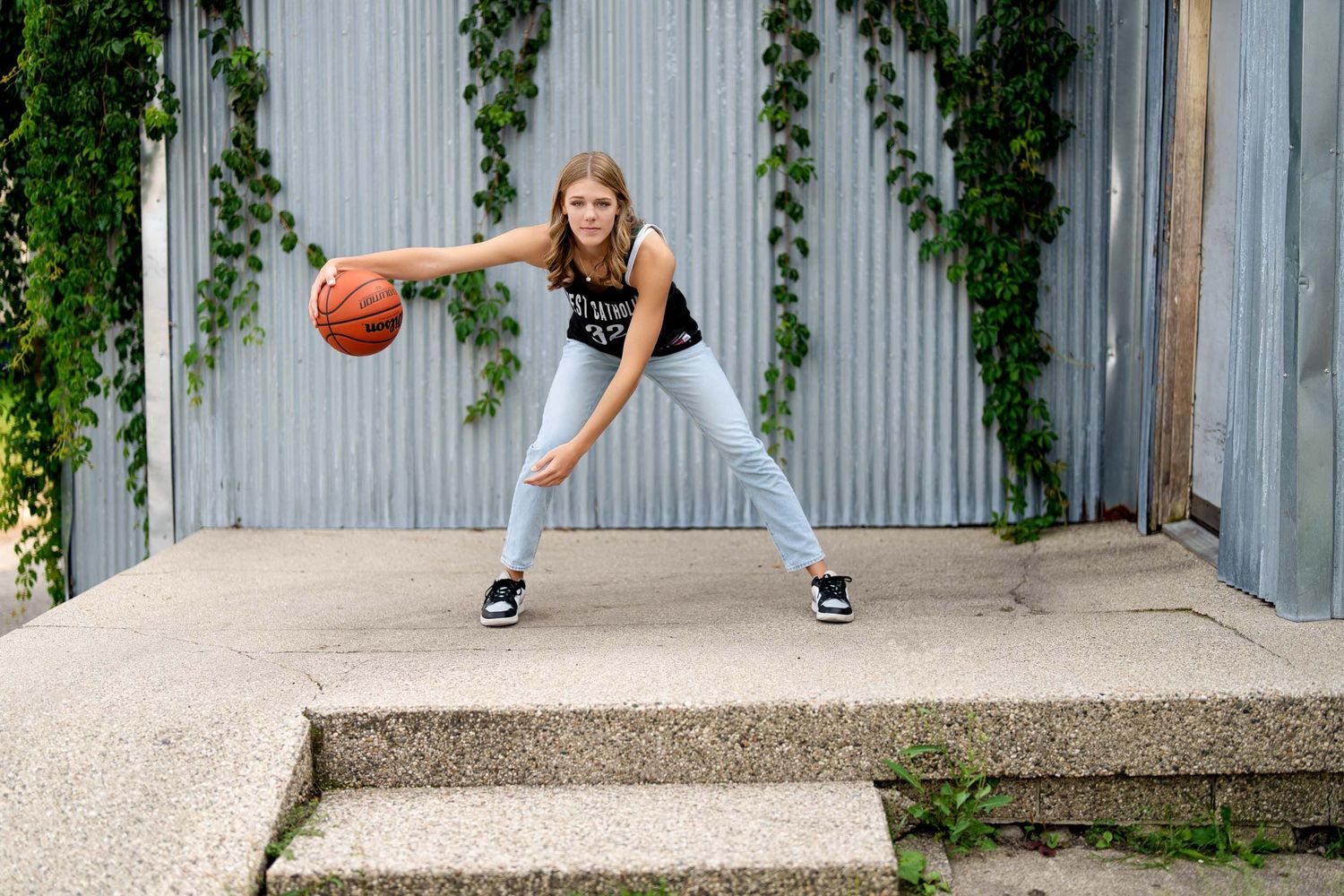 Basketball player dribbling and practicing moves against a white wall with ivy.