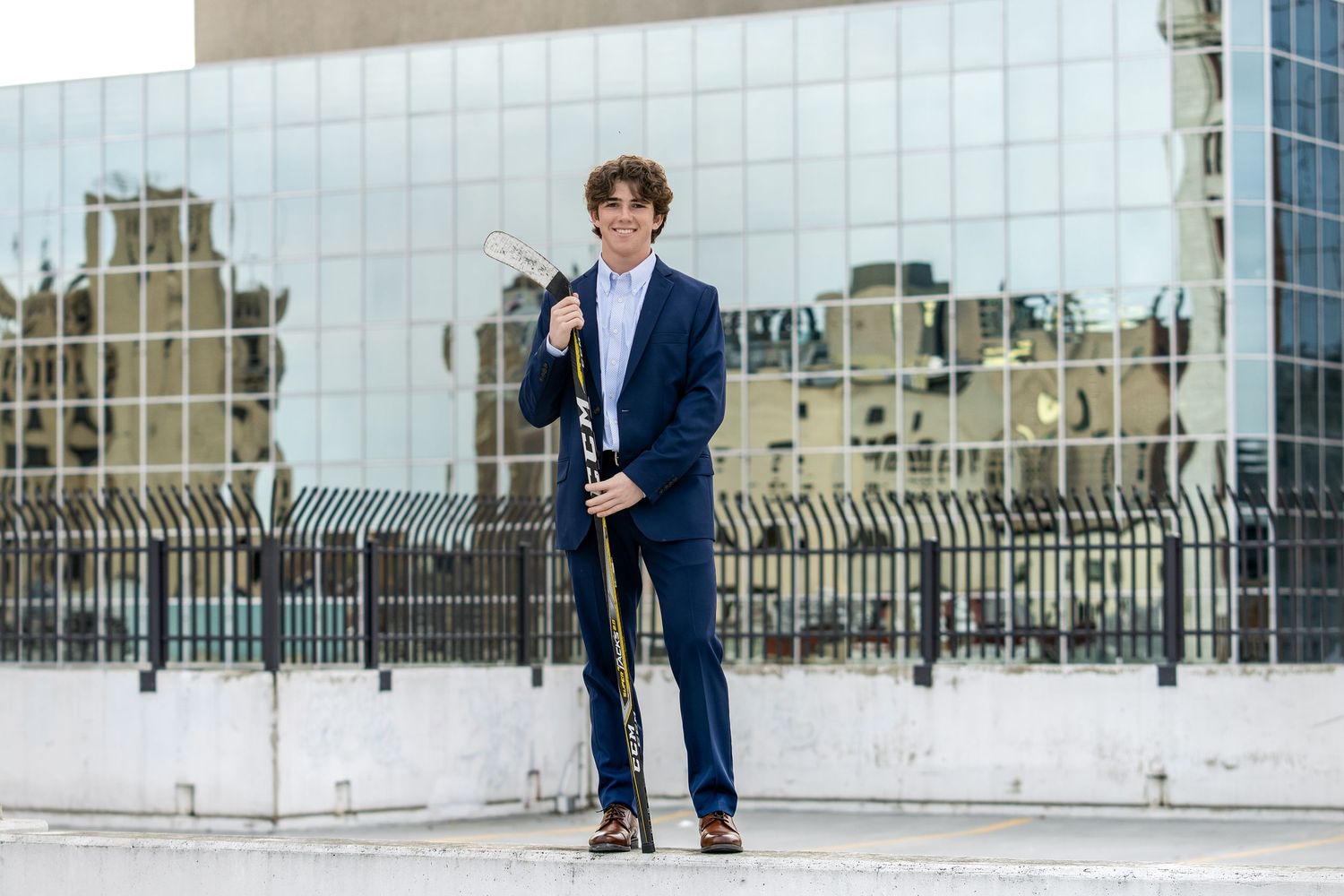 A musician in a navy suit poses with a saxophone against a modern building facade.
